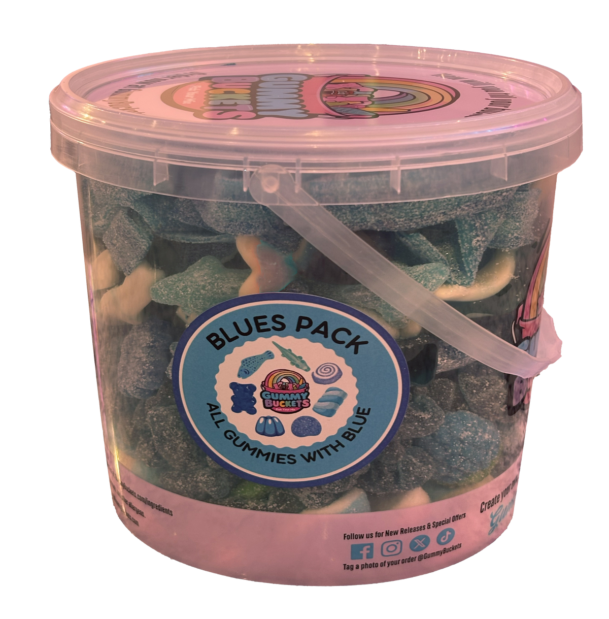 A clear plastic tub filled with assorted blue and green sugar-coated gummy candies, labeled 'Blues Pack' by Candy Cakes Creamery. The tub has a pink lid and a clear plastic handle.