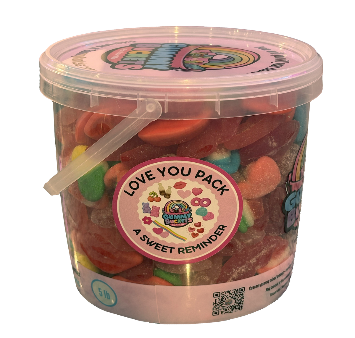 A 5-liter clear plastic tub filled with assorted colorful gummy candies, featuring a round pink and white 'Love You Pack' sticker on the front. The tub has a clear lid with a cartoon character illustration and a small clear plastic handle.