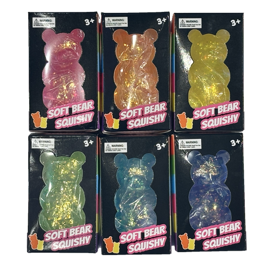 Six packaged soft sparkle bear squishy toys arranged in a 2x3 grid on a white background. Each bear-shaped toy is inside a black retail box with a colorful pink 'SOFT BEAR SQUISHY' label and age warning stickers.  Pink, orange, yellow, green, blue and purple.