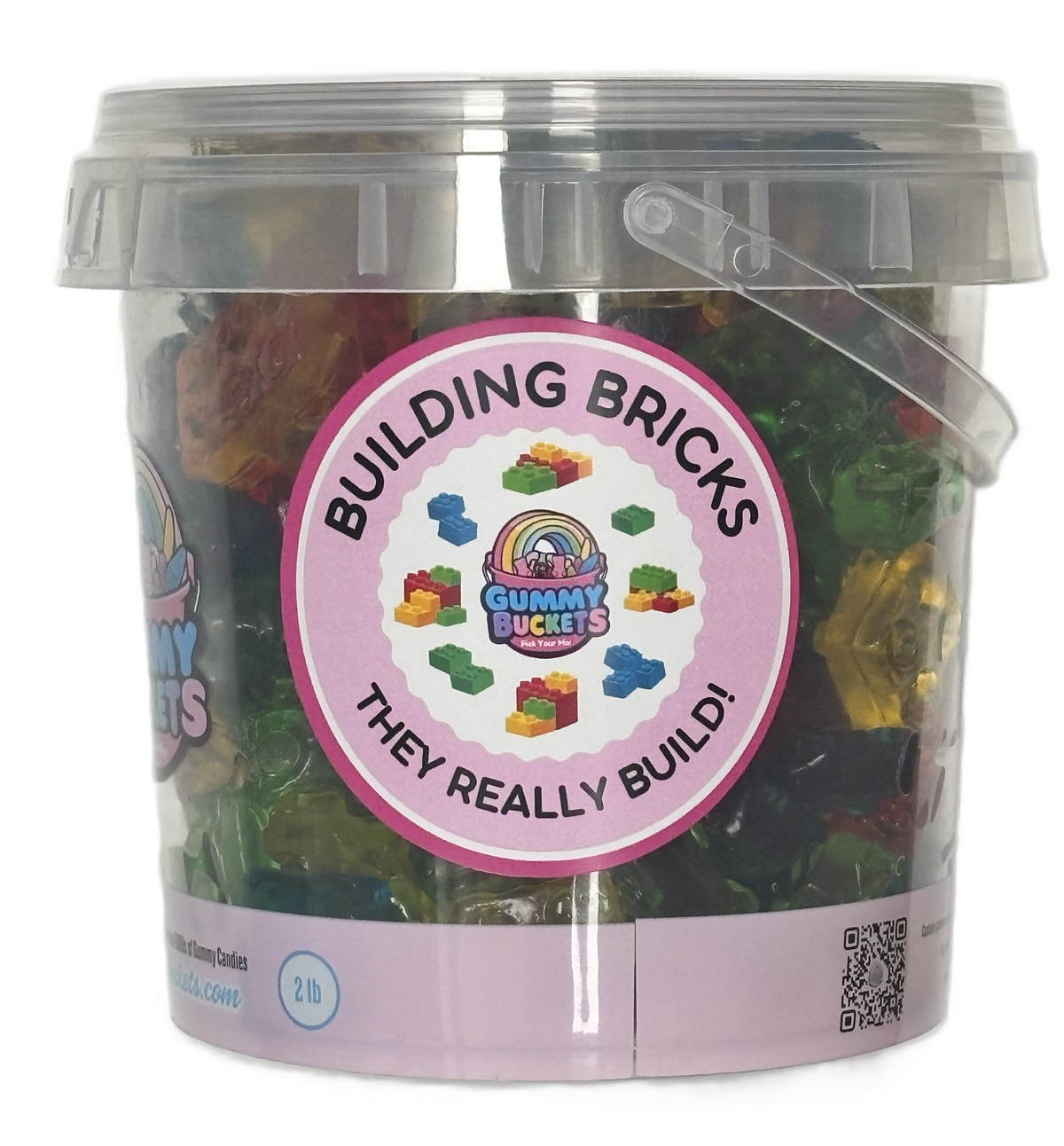 A clear plastic bucket filled with assorted gummy candies, featuring a large pink circular label that reads 'BUILDING BRICKS THEY REALLY BUILD!' with the Gummy Bucket logo. The bucket has a translucent lid and a clear plastic handle, set against a plain white background.