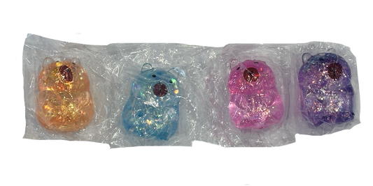 Four small glittery bear-shaped items in different colors, each individually wrapped in clear plastic packaging, arranged in a row against a white background. Orange/brown, blue, pink and purple glittery options.
