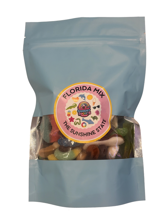 A light blue resealable stand-up pouch with a clear window showing a colorful assortment of Florida-themed gummy candies including sharks, alligators, starfish, and tropical shapes inside. A round pink and yellow label on the front reads 'FLORIDA MIX' and 'THE SUNSHINE STATE' with the Gummy Buckets logo surrounded by illustrated Florida icons in the center.