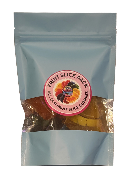 A light blue resealable stand-up pouch with a clear window showing large fruit slice gummy candies in orange, red, yellow, and black inside. A round pink label on the front reads 'FRUIT SLICE PACK' and 'ALL OUR FRUIT SLICE GUMMIES' with the Gummy Buckets logo surrounded by illustrated fruit slice candy icons in the center.