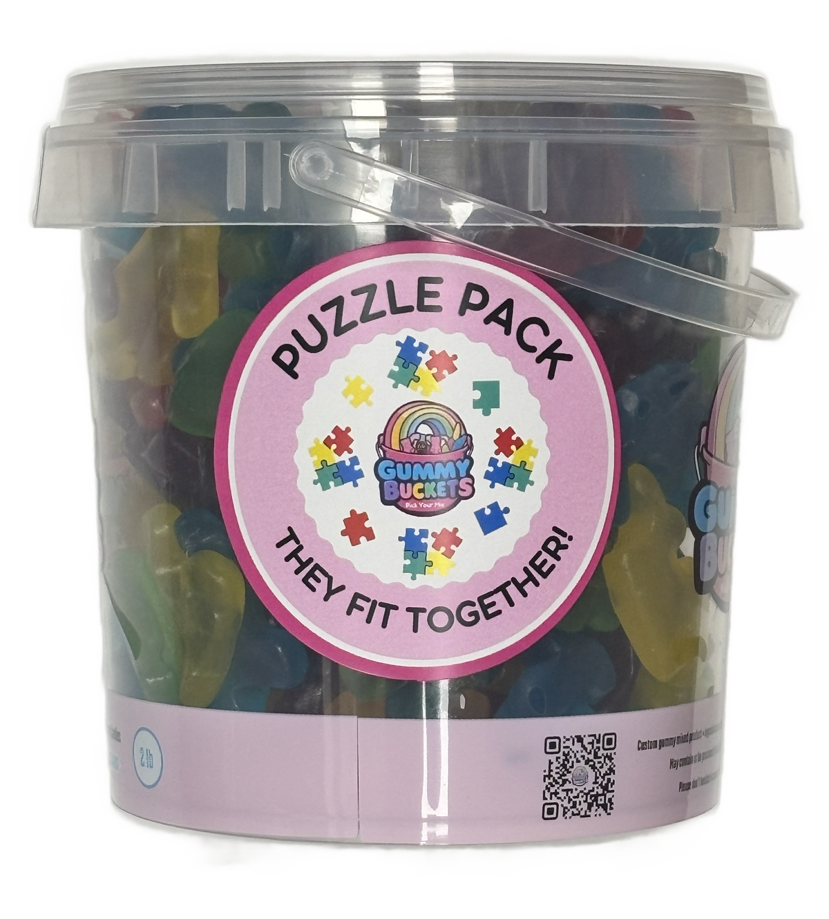 A clear plastic bucket filled with assorted gummy candies, featuring a round pink label that reads 'PUZZLE PACK THEY FIT TOGETHER!' with a rainbow and puzzle-piece design. The Gummy Bucks logo is visible on the label.