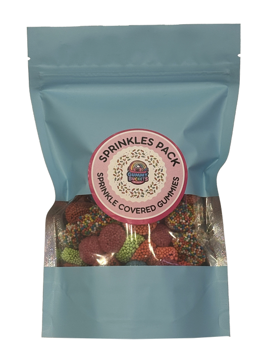A light blue resealable stand-up pouch with a large clear window showing round gummy candies coated in colorful sprinkles in red, green, orange, and yellow inside. A round pink label on the front reads 'SPRINKLES PACK' and 'SPRINKLE COVERED GUMMIES' with the Gummy Buckets logo surrounded by illustrated sprinkle details in the center.