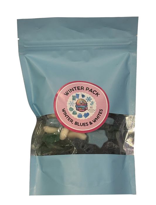 A light blue resealable stand-up pouch photographed on a marble countertop with a clear window showing blue, white, and silver winter-themed gummy candies including snowflake shapes, white bears, and sugared blue gummies inside. A round pink label on the front reads 'WINTER PACK' and 'WINTER, BLUES & WHITES' with the Gummy Buckets logo surrounded by illustrated snowflake and winter candy icons.